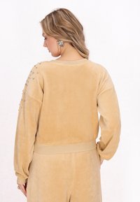Beige, puha szövet pulóver kerek nyakkivágással, hosszú ujjakkal és szegecsekkel díszített vállakkal.