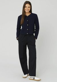 Cardigan texturé bleu marine avec col rond et devant boutonné, associé à un pantalon noir à rayures et des baskets blanches avec des accents noirs.