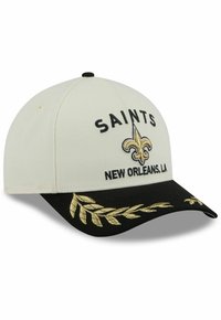 White cap with black bill, features "SAINTS" and fleur-de-lis logo in gold embroidery, adorned with gold leaf pattern on the brim.