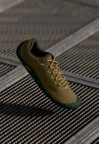 Calzado con parte superior de malla en verde oliva y marrón amarillento, cordones a juego y una suela de goma texturizada. Marca Vibram visible.