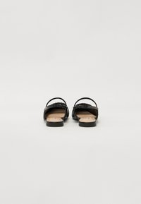 Sandales plates noires avec une tige en cuir lisse, dos ouvert et fine bride de cheville ; semelle plate et subtil détail de couture décorative.