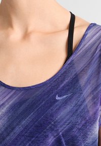 Close-up van een persoon die een paarse Nike mesh top draagt over een zwarte band, waarbij een deel van de nek en schouder zichtbaar is.