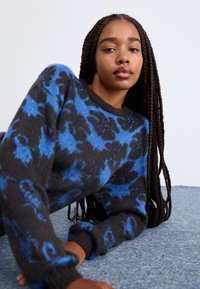 Maglione a righe nero e blu con maniche lunghe, colletto rotondo e polsini a coste, caratterizzato da una texture morbida e un motivo floreale.