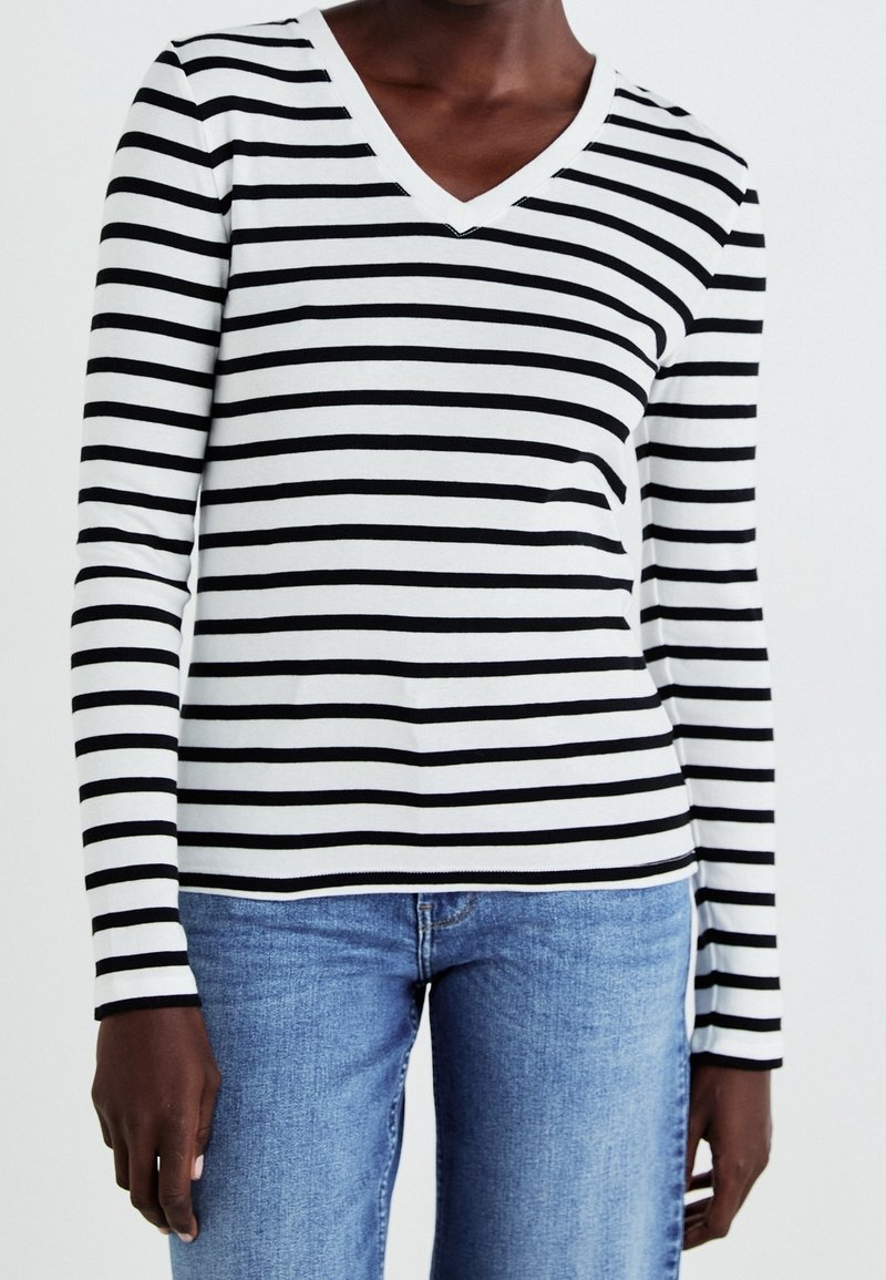 Haut à manches longues rayé noir et blanc avec encolure en V, fabriqué en tissu doux. Associé à un jean en denim bleu.