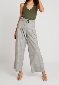 Beige och grå rutiga vida byxor med hög midja och spänne, kombinerade med en mörkgrön tanktopp och ljusa sandaletter med remmar.