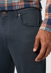 Ciemnoniebieskie spodnie slim fit, wykonane z gładkiego materiału, z kieszenią z przodu, subtelnym przeszyciem oraz metalowym detalem na guzik.