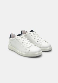 Sneakers in pelle bianca con lati perforati, punta rotonda, lacci piatti e un'accento blu navy sul tallone. Texture liscia, design minimalista.