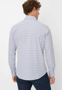 Weißes Langarmhemd mit einem mehrfarbigen Blumenmuster; glatte Textur; klassischer Kragen und geknöpfte Manschetten. Getragen mit dunklen Jeans.