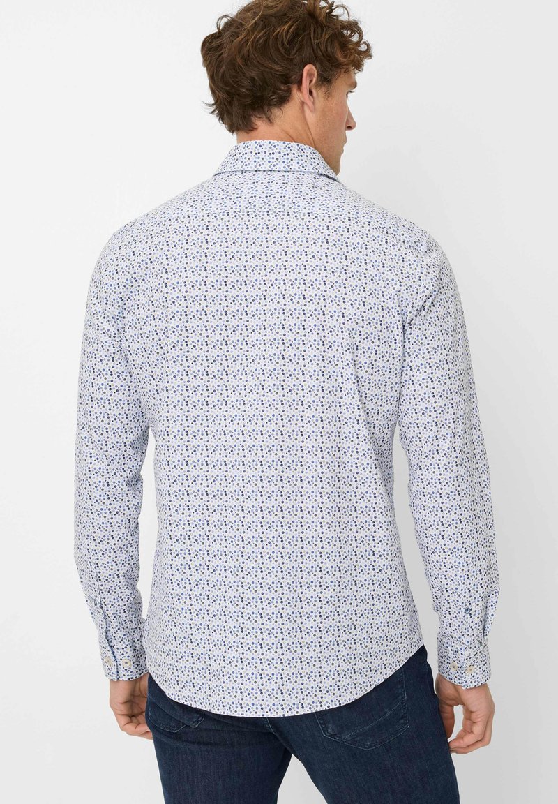 Weißes Langarmhemd mit einem mehrfarbigen Blumenmuster; glatte Textur; klassischer Kragen und geknöpfte Manschetten. Getragen mit dunklen Jeans.