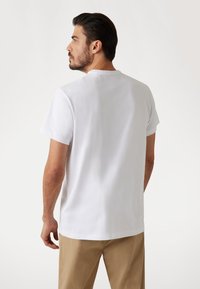 Weißes Baumwoll-T-Shirt mit kurzen Ärmeln, Rundhalsausschnitt und lockerem Schnitt. Glatte Textur mit schlichter Gestaltung, von hinten präsentiert.