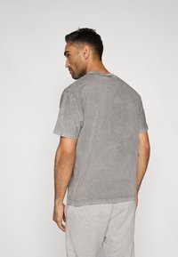 Šedé tričko s krátkým rukávem z měkké látky, s kulatým výstřihem a mírně vypranou texturou, doplněné šedými tepláky.