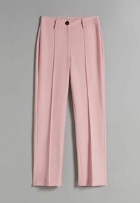 Světle růžové kalhoty na míru s předním záhybem, poutky na opasek a černým knoflíkovým zapínáním, vystavené na šedém pozadí.