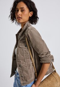 Olivgrön cordjacka med knäppning fram, bröstficka och uppvikta ärmar. Ett par ljusblå jeans och en beige axelväska.