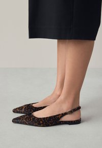 Chaussures plates slingback à imprimé léopard avec bouts pointus, en tissu texturé. Elles présentent une bride fine autour de la cheville avec une boucle carrée en accent.