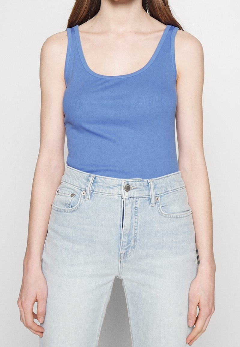 Blå ribbad linne med en rundad halsringning, ihop med ljusblå high-waisted jeans; figurnära design och mjuk textur.