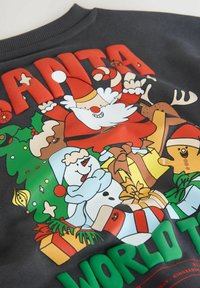 Czarny sweatshirt z kolorowym rysunkowym wzorem przedstawiającym Świętego Mikołaja, bałwanka, pierniczka i pudełek z prezentami. Napis nawiązuje do "ŚWIATOWA TRASA ŚWIĘTEGO MIKOŁAJA".
