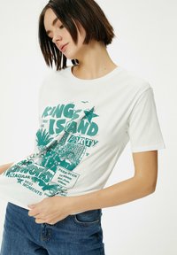 Hvid bomulds t-shirt med grøn grafisk design, der inkluderer tekst og illustrationer, korte ærmer og rund halsudskæring. Casual pasform.