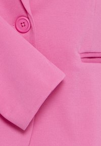 Rosa Blazer-Stoff mit strukturierter Oberfläche, versehen mit einem runden rosa Knopf und einer kleinen Seitentasche. Der Ärmel ist leicht hochgeschlagen.