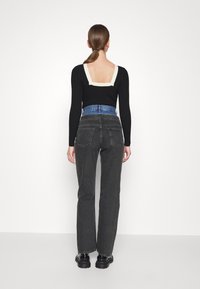 Top negro de manga larga con textura acanalada y un recorte cuadrado en crema, combinado con unos vaqueros negros de talle alto, que presentan un detalle azul en la cintura.