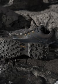 Chaussures de randonnée foncées avec des semelles en caoutchouc Continental texturées reposant sur un sol rocheux humide.