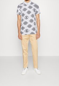 Kortärmad polo skjorta i ljusgrått med svart glob- och logomönster.  Kombination med beige byxor och vita sneakers. Slät textur.