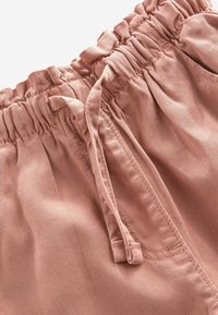 Pantaloni shorts in tessuto rosa con una cintura elastica testurizzata e un cordoncino abbinato, che mostrano un materiale liscio e una delicata lucentezza.