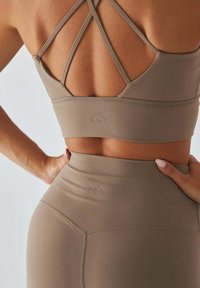 Beżowy krótki top sportowy z krzyżującymi się tylnymi ramiączkami oraz legginsy z wysokim stanem, z delikatnym logo serca i gładką fakturą.