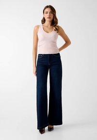 Débardeur côtelé rose clair associé à un jean large bleu foncé. Le débardeur présente un col en V, tandis que le jean est taille haute avec une finition minimaliste.