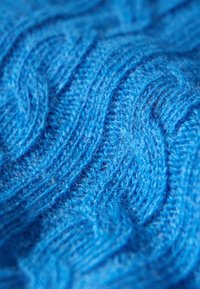 Blått stickat tyg med en strukturerad kabelmönster som visar en mjuk och fluffig yta med intrikata vågformade designer.