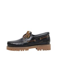 Bateau en cuir noir avec des lacets marron et une semelle en caoutchouc tan robuste, couture latérale et œillets en métal.