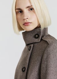 Manteau en laine marron avec un col montant, doté de boutons noirs et d'une coupe ajustée. Texture lisse et design minimaliste.