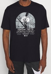 Camiseta negra de algodón con un gráfico central de un aro de baloncesto y ramas de árbol, con el texto "Just Do It" y "Nike Nets Basketball".