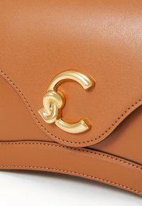 Smeđa kožna torba s zlatnim međusobno povezanim "C" logotipom i zakrivljenim šavovima na preklopu. Glatka tekstura.