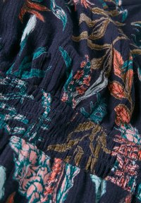 Tejido de navy oscuro con un patrón floral en rosa, verde azulado y dorado. La textura es suave con detalles de elástico fruncido.