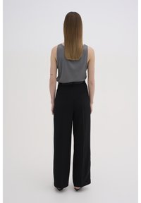 Un tricou gri cu nervuri, purtat cu pantaloni negri cu talie înaltă și croială largă; material neted cu o siluetă elegantă și buzunare mici în partea din spate.