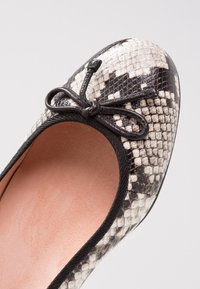 Ballet flat with a black and white snake print, rounded toe, and a black bow accent. Soft inner lining and textured exterior.