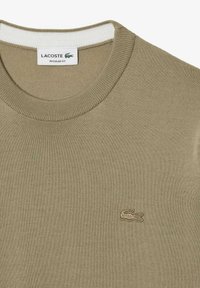 Khaki sweter z prążkowanym okrągłym dekoltem, ozdobiony małym haftowanym logo na piersi, wykonany z teksturowanego materiału. Krój o regularnym dopasowaniu.