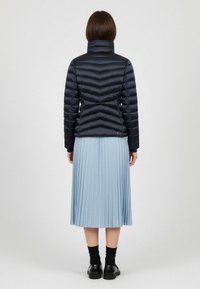 Chaqueta acolchada de punto navy con acolchado en forma de chevron, cuello alto y puños acanalados, combinada con una falda plisada azul clara y zapatos negros.