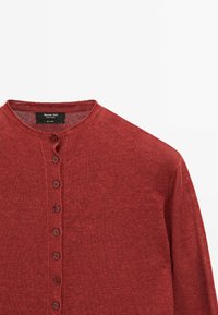Cardigan en lin rouge avec un col rond et une rangée verticale de petits boutons assortis sur le devant.