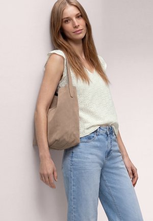 Młoda kobieta o długich blond włosach, ubrana w biały bezrękawnik, jasnoniebieskie dżinsy i niosąca beżową torbę na ramię.