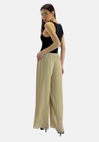 Zwarte mouwloze top gecombineerd met geplooide beige wijde broek. De broek heeft een elastische tailleband en een soepele, vloeiende textuur.