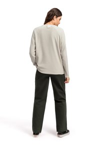 Maglietta grigia chiara a maniche lunghe con orlo arrotondato e maniche raglan, abbinata a pantaloni larghi verde scuro e scarpe da ginnastica nere.