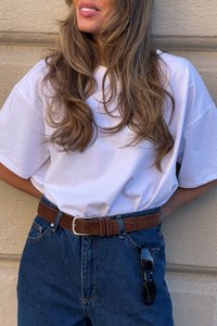 White oversized t-shirt with short sleeves, paired with high-waisted blue denim jeans and a brown leather belt. Black sunglasses attached.