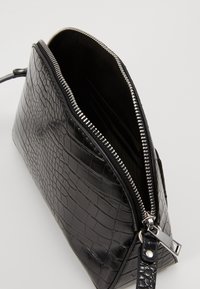 Borsa in pelle nera con stampa coccodrillo, chiusura con zip, forma angolare e dettagli in metallo argentato. Tessuto liscio con scomparti interni.