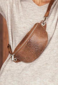 Brown faux leather fanny pack with textured snake pattern, silver zipper, and adjustable strap, worn across the waist against a light sweater.