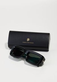 Ochelari de soare pătrați cu rame negre lucioase și lentile verde închis. Împreună cu o carcasă din piele neagră cu branding auriu.