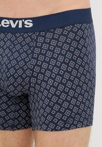 Námorné modré boxerky so geometrickým bielym vzorom. Majú elastický pás s logom "Levi's" v sivej farbe. Hladký povrch.