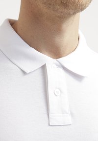 Camisa polo blanca con una tela texturada y transpirable. Cuenta con un collar clásico y una tapeta de tres botones con botones blancos.