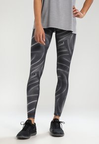 Leggings de colores negro y blanco con un diseño de espiral dinámico, tejido elástico y un ajuste ceñido, combinados con zapatillas deportivas negras.