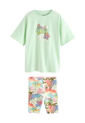 Hellgrünes Baumwoll-T-Shirt mit buntem Schriftzug und Blumendesigns, kombiniert mit weißen Leggings mit lebendigen Mustern und Text.